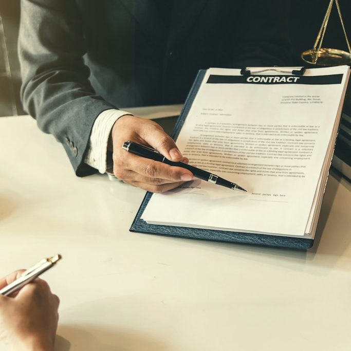 Zwei Hände über einem Vertrag, eine hält einen Stift, die andere macht Notizen.